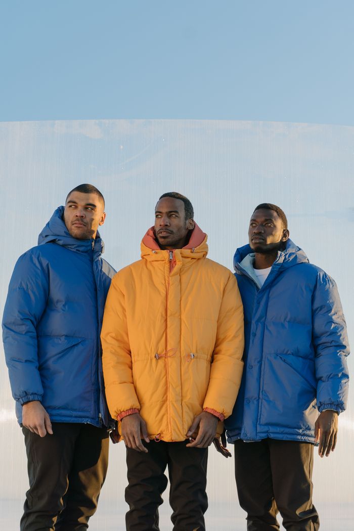 Three diverse male models wearing winter jackets, posing against a clear blue sky.